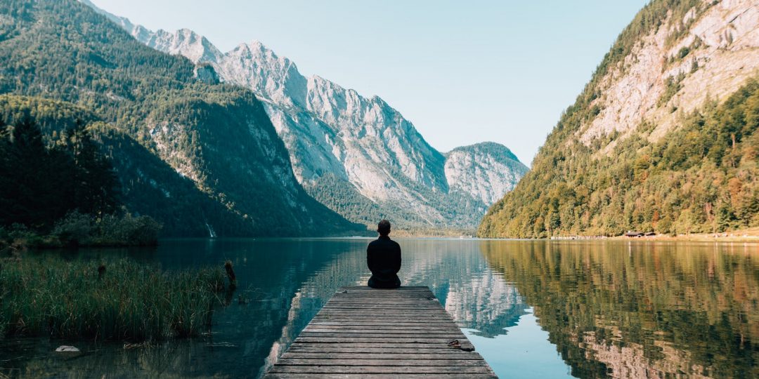a person sitting on wooden planks across the lake scenery